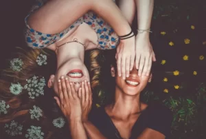 two women lyind down with their hands over each others eyes