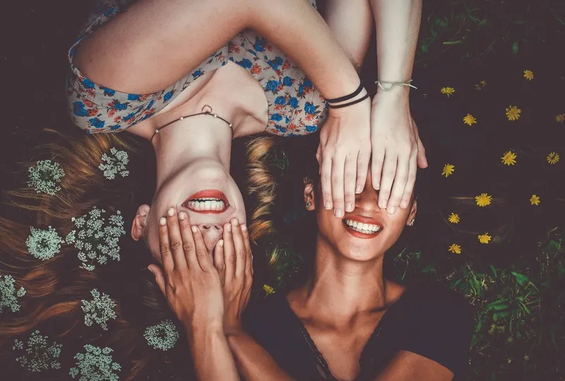 two women lyind down with their hands over each others eyes