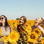 three women in a sunflower field laughing and having a converstaion on a sunny day