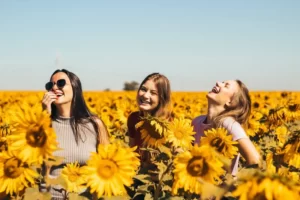three women in a sunflower field laughing and having a converstaion on a sunny day