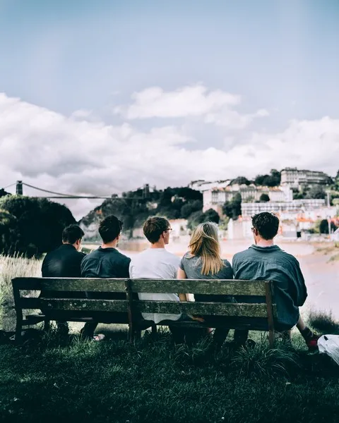 five friends sat on a wooden bench viewed from behind and looking out over towards a city - social capital