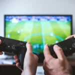 Two controllers in front of a TV playing a football game