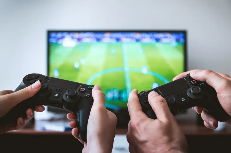 Two controllers in front of a TV playing a football game