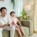 A father and son playing video game sat on the couch.