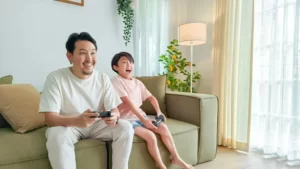 A father and son playing video game sat on the couch.