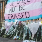 A trans movement flag with the words 'we will not be erased'
