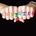 a persons's fists with the letters LGBTQIA+