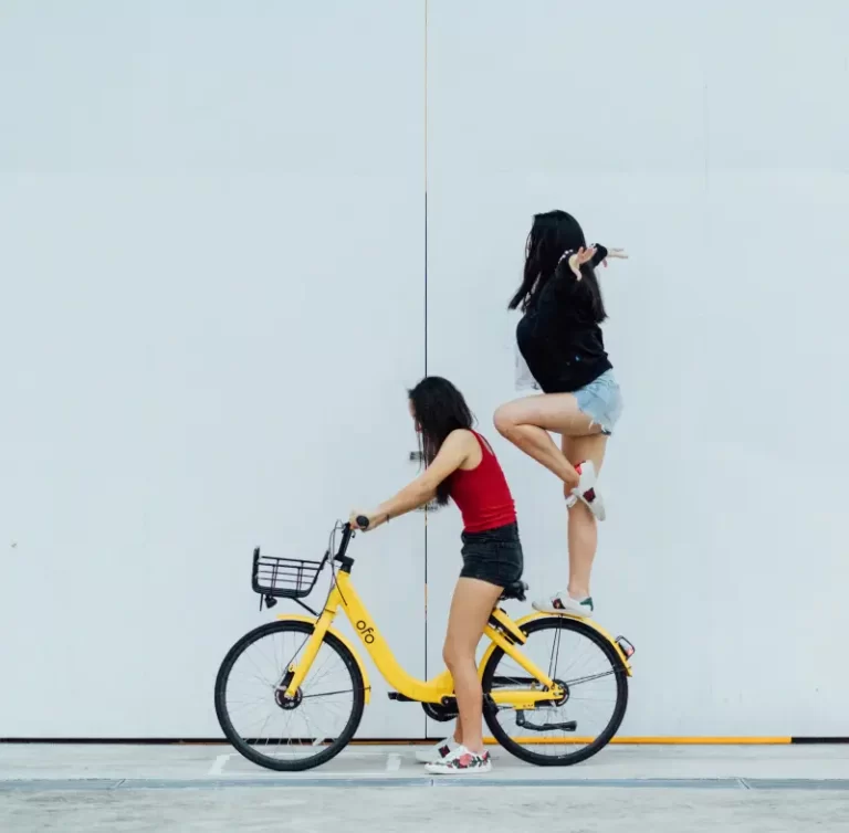 two women riding a bike - one stood on the back wheel - feminism