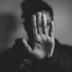 black and white image of a person holding their hand in front of their face to symbolise identity oppression