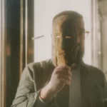 a man holding a wooden mask in front of his face