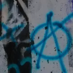 A blue anarchism symbol wirtten on a wall in graffiti