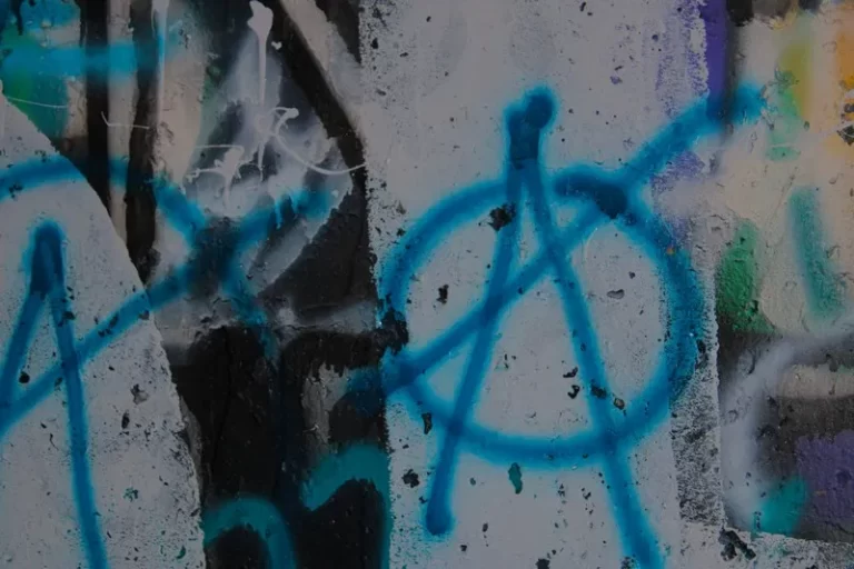 A blue anarchism symbol wirtten on a wall in graffiti
