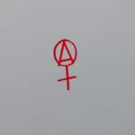 an anarchist ideology symbol in red on a white wall