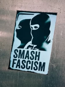 A sign with two people wearing balaclavas with the words 'smash fascism'.