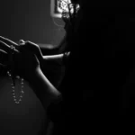 black and white silhouette of woman holding rosary beads