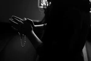 black and white silhouette of woman holding rosary beads