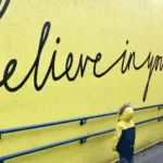 a small boy looking at a yellow wall with the words 'believe in yourself' - self-concept