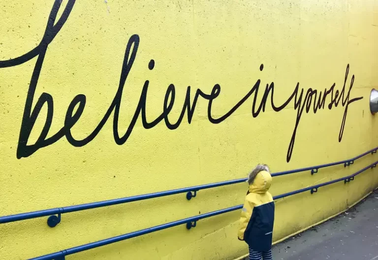 a small boy looking at a yellow wall with the words 'believe in yourself' - self-concept