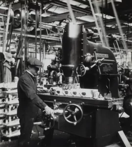 a black and white shot of a man wearing a flat cap operating a historical machine
