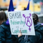 a protestor holding a placard saying 'smash the patriarchy and capitalism'