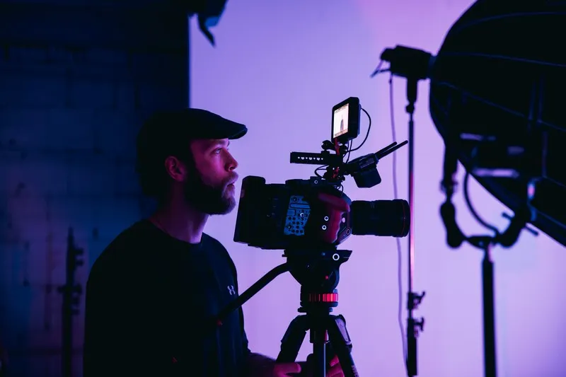 A man behind a TV camera in front of a dimmed purple background.