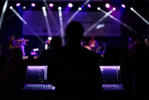 A music producer stood at a mixing desk against a purple lighted background stage lights