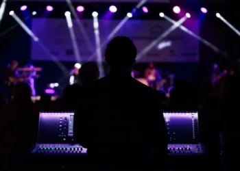 A music producer stood at a mixing desk against a purple lighted background stage lights