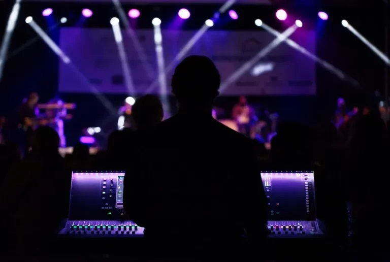 A music producer stood at a mixing desk against a purple lighted background stage lights