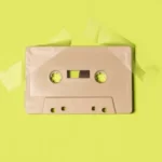 A beige cassette tape attached to a yellowy-green background with sticky tape