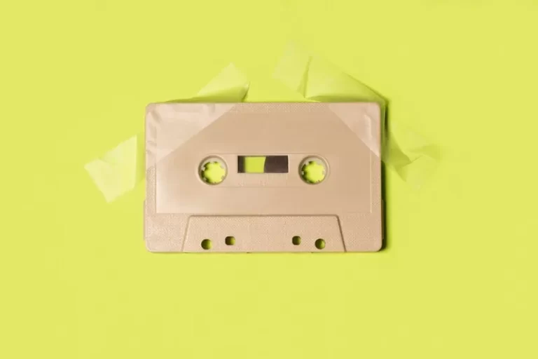 A beige cassette tape attached to a yellowy-green background with sticky tape