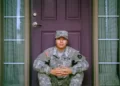 a soldier sat on the door step in front of a front door. Militarism.