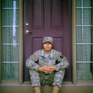 a soldier sat on the door step in front of a front door. Militarism.