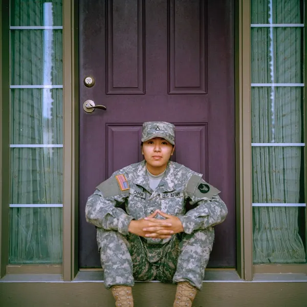 a soldier sat on the door step in front of a front door. Militarism.