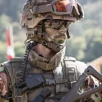 A close up of a soldier wearing sunglasses and carrying a gun