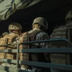 three soldiers viewed from behind sat on a militray vehicle