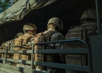 three soldiers viewed from behind sat on a militray vehicle