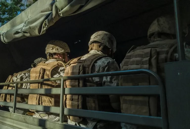 three soldiers viewed from behind sat on a militray vehicle