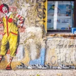 a graffitti image on a wall of ronald mcdonald - capitalism