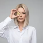 A female entrepreneur in a white blouse holding a coin to her eye