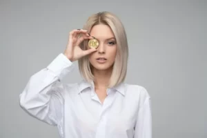 A female entrepreneur in a white blouse holding a coin to her eye