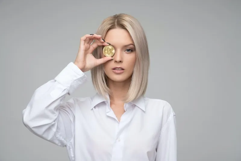 A female entrepreneur in a white blouse holding a coin to her eye