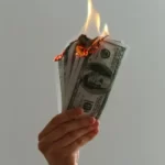a hand holding a bundle of dollar bills on fire