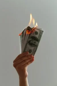 a hand holding a bundle of dollar bills on fire