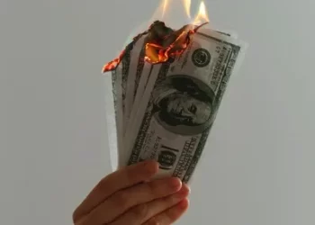 a hand holding a bundle of dollar bills on fire