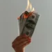 a hand holding a bundle of dollar bills on fire