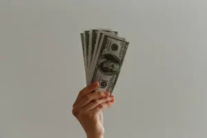 A hand offering a wad of dollar bills against a grey background