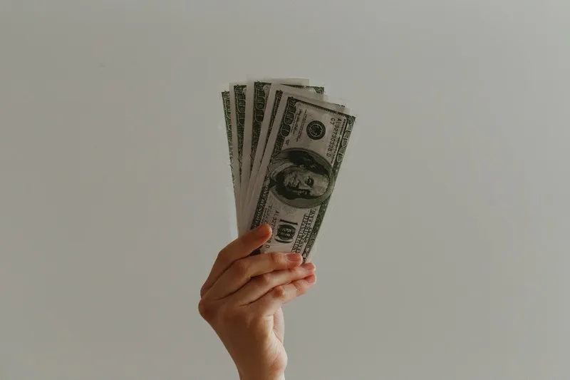 A hand offering a wad of dollar bills against a grey background