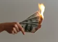 A hand holding a bunch of dollar bills on fire