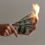 A hand holding a bunch of dollar bills on fire