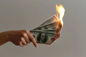 A hand holding a bunch of dollar bills on fire